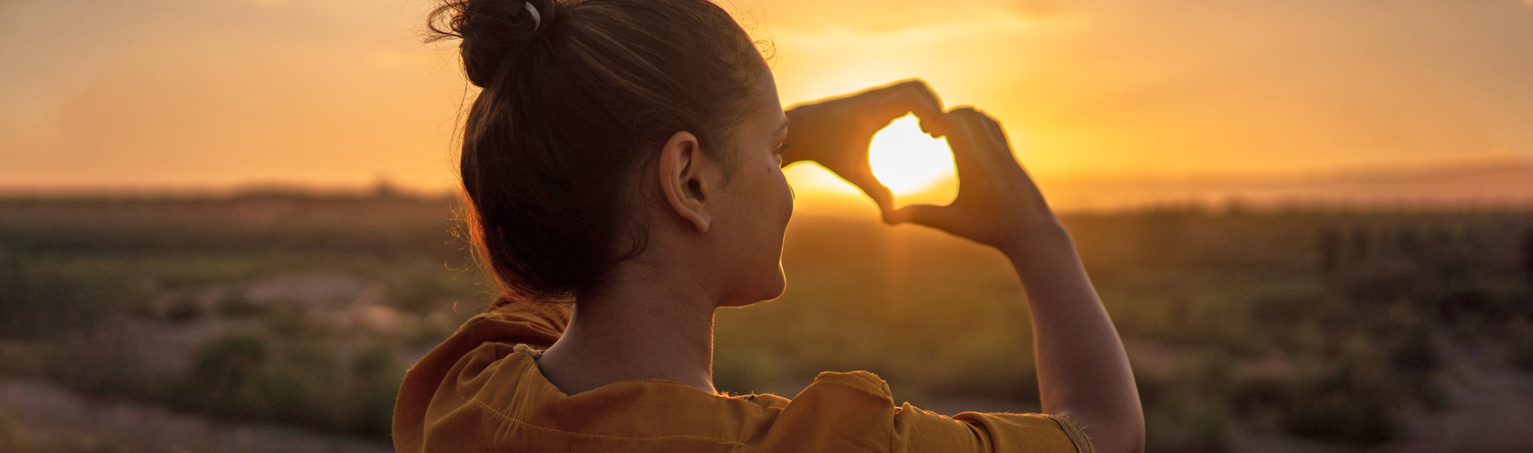 Woman shaping hands into heart shape over sunset