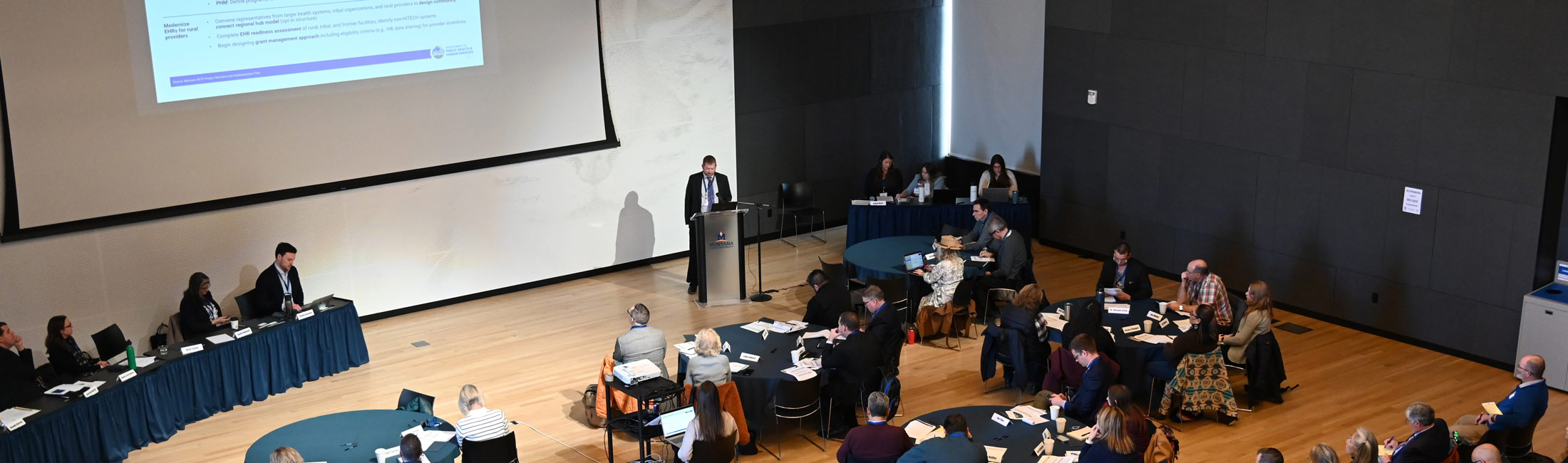 Man speaking at event in front of projector screen