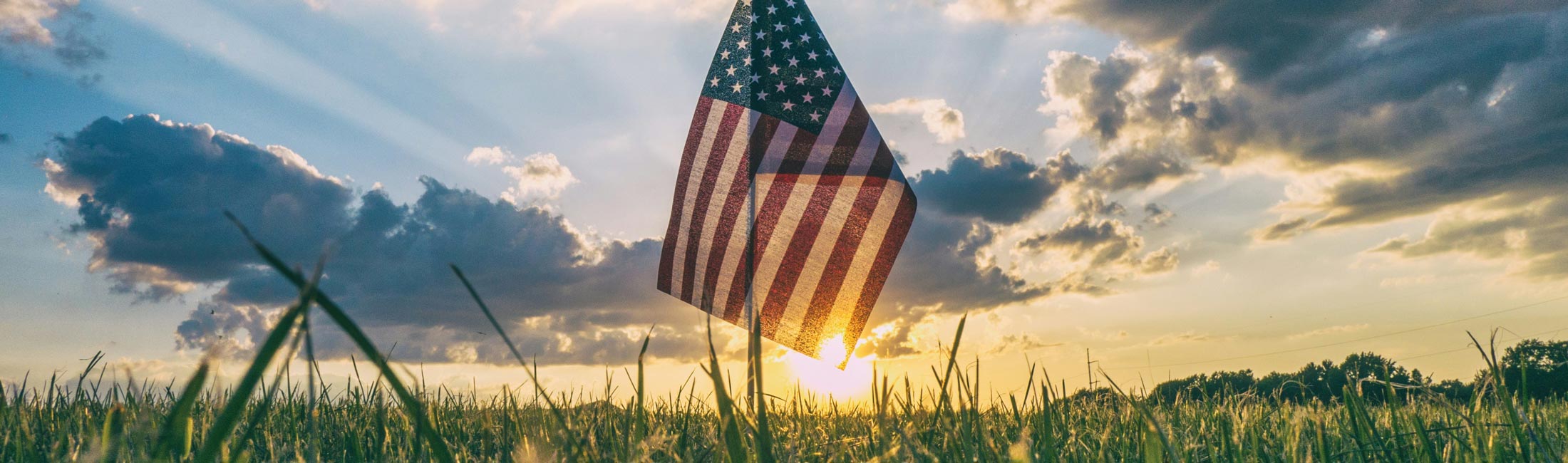 Small flag in the grass with the sun behind it