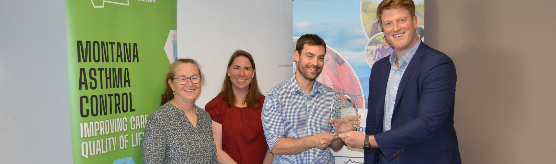 People standing in front of banners, at left, EPA Regional Administrator Cyrus Western presents BJ Biskupiak of DPHHS with the 2025 National Environmental Leadership Award in Asthma Management. Pictured below is the Montana Asthma Control Program team