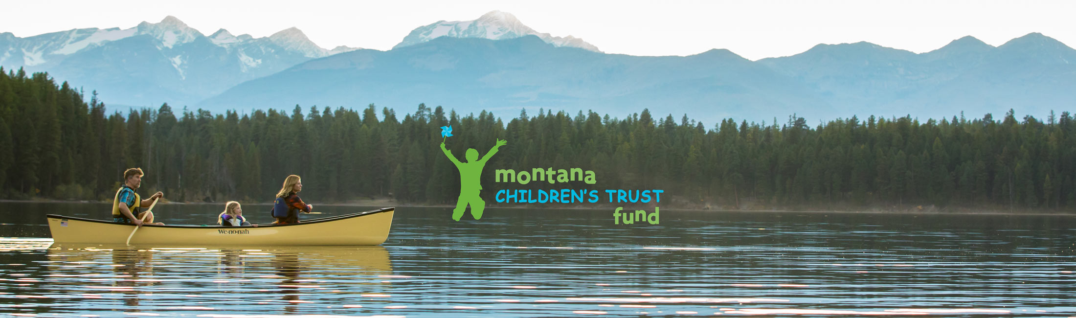 family paddling in canoe with mountains in background