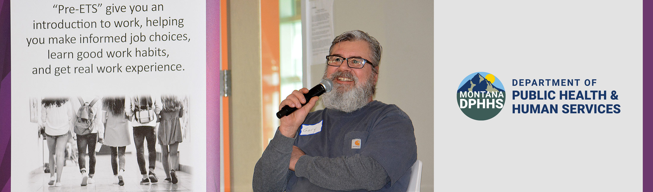 Man seating speaking into microphone with pull-up banner for Vocational Rehab and Blind Services
