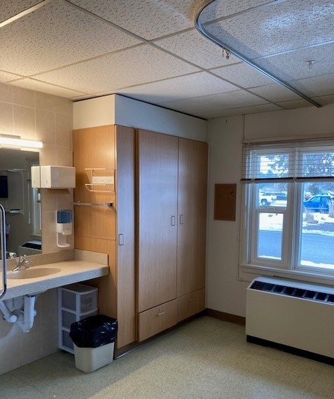A picture of the sink and cabinet in a resident room. The cabinet is brown, with three doors and two drawers. There is also a window looking into the parking lot.