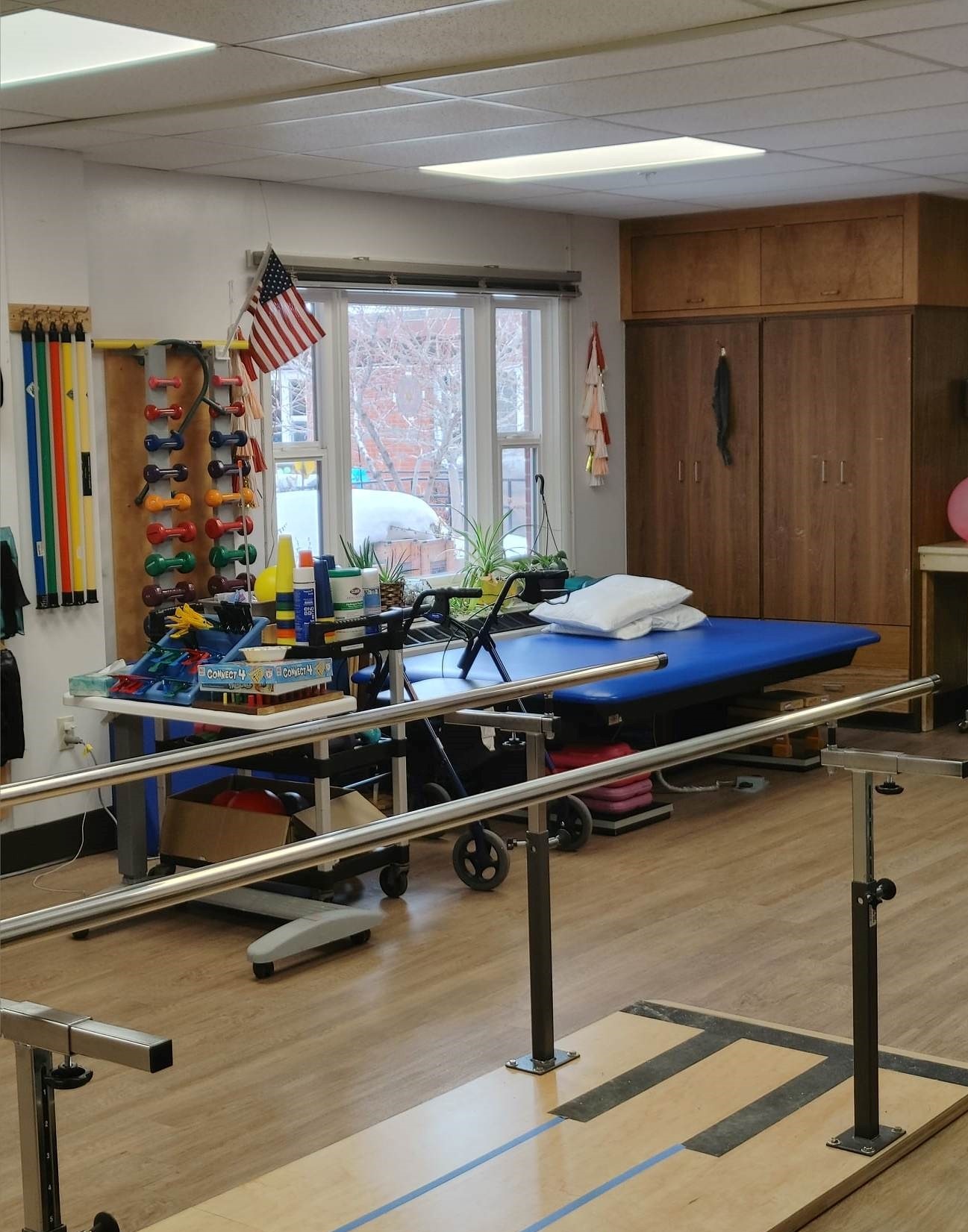 A picture of the therapy room. There is a window, weights, and other fitness and therapy tools. There are also games, such as connect 4.
