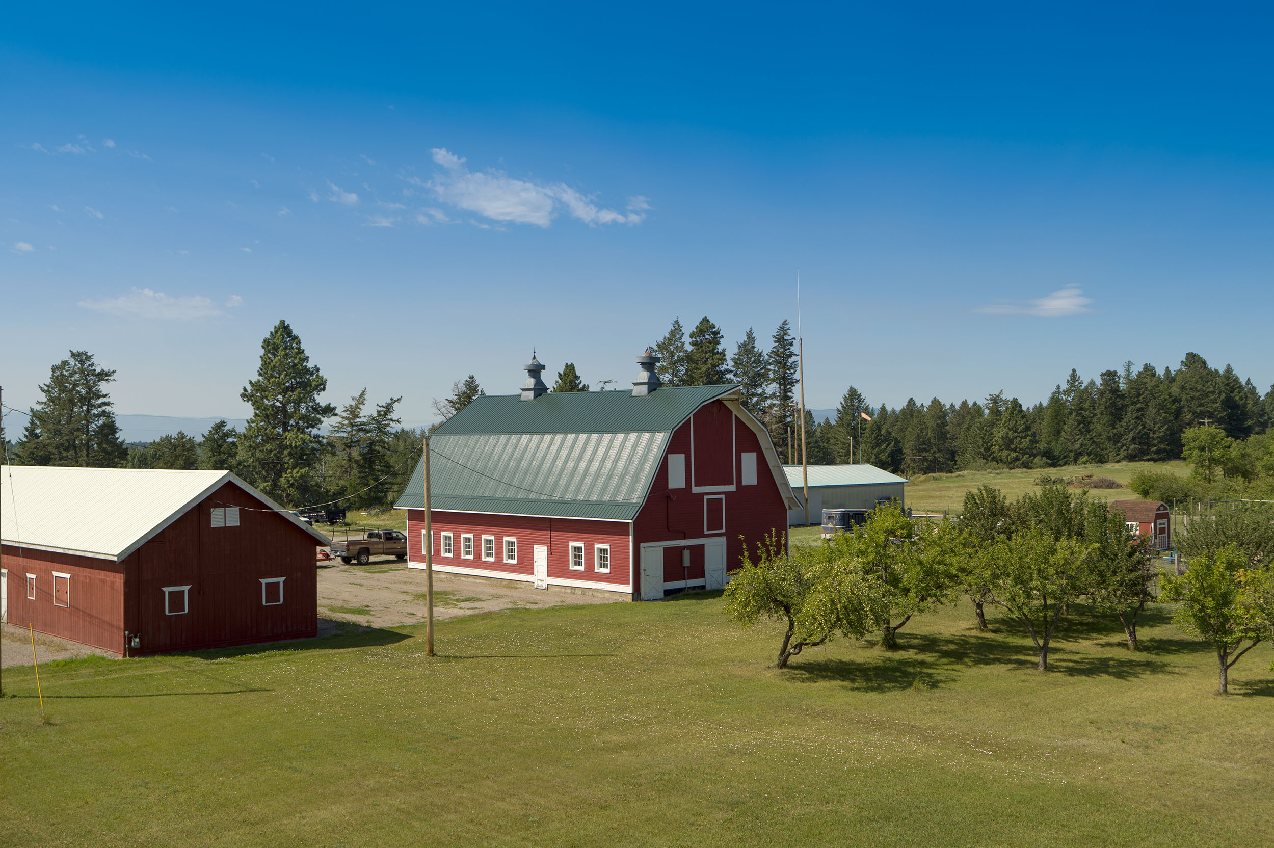 A picture of the barn on the Montana Veterans home grounds. It is surrounded by a large open green field with trees in the background.