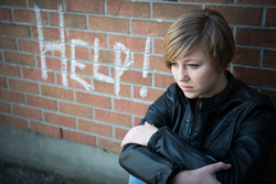 Child sitting by a brick wall with the words help painted on the brick