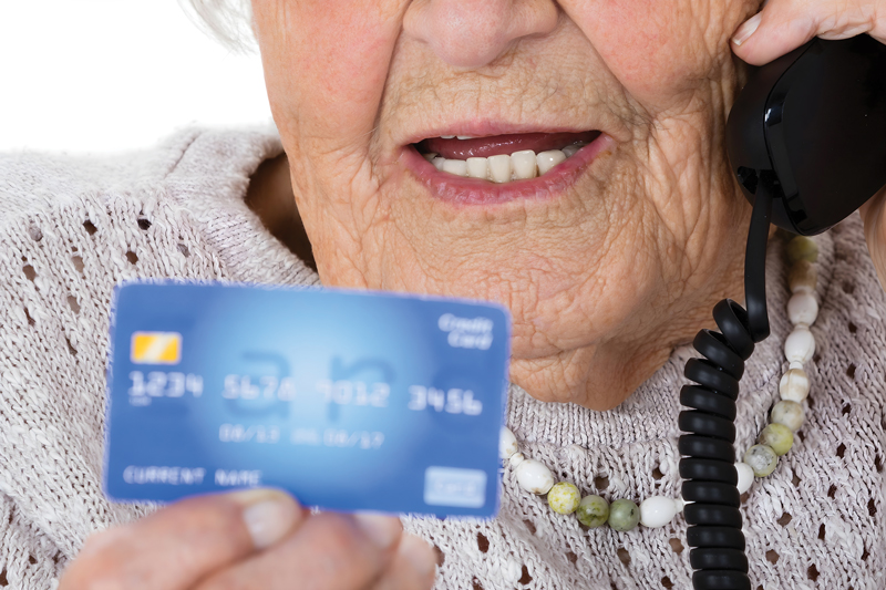 Photo of an elderly woman on the phone and holding a credit card